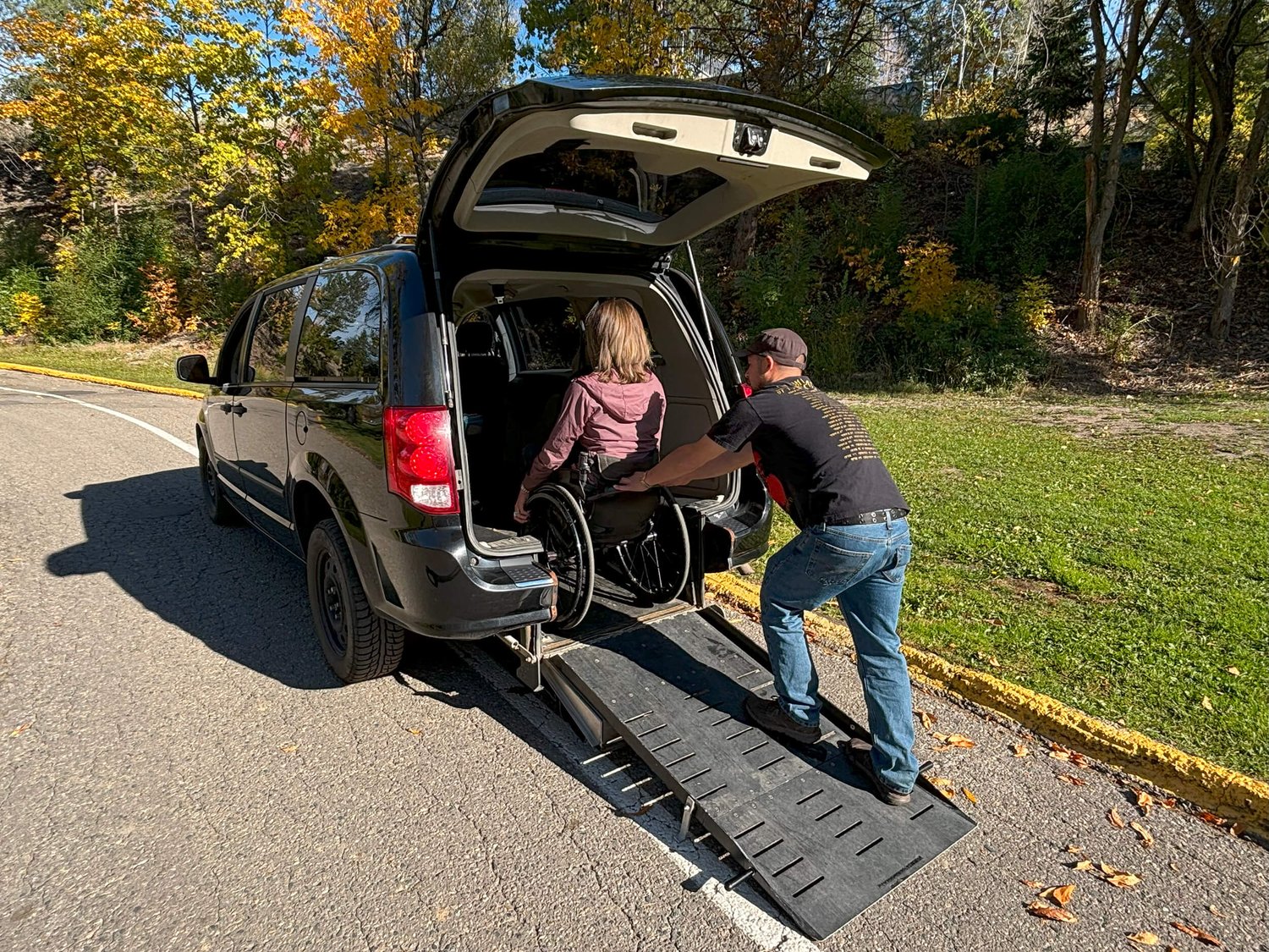 A NOW Shuttle driver assisting a passenger using a wheelchair into an accessible vehicle.