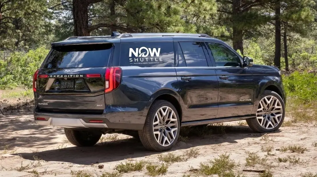 A NOW Shuttle branded SUV parked among pine trees