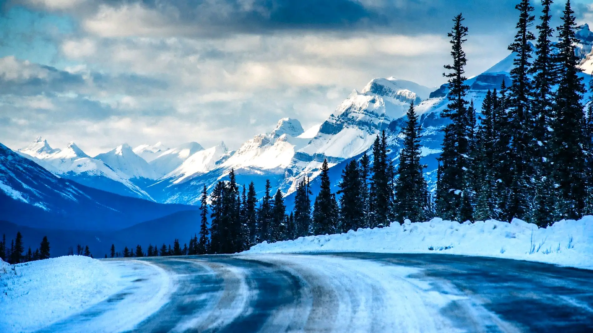 A snow-covered mountain highway curving toward snowy peaks